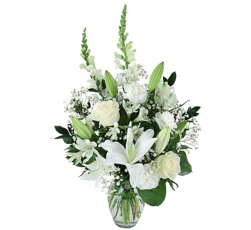 Tall white arrangement with lilies, roses, carnations, and snapdragons in a clear glass vase