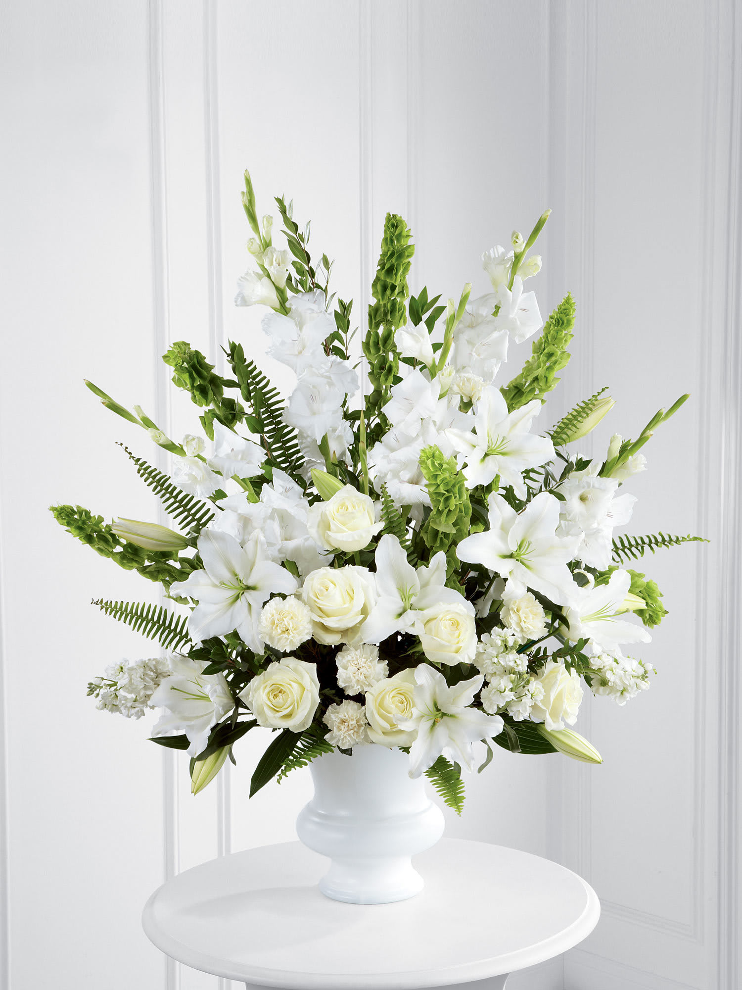 Tall white arrangement of lilies, roses and carnations in a white pedestal vase