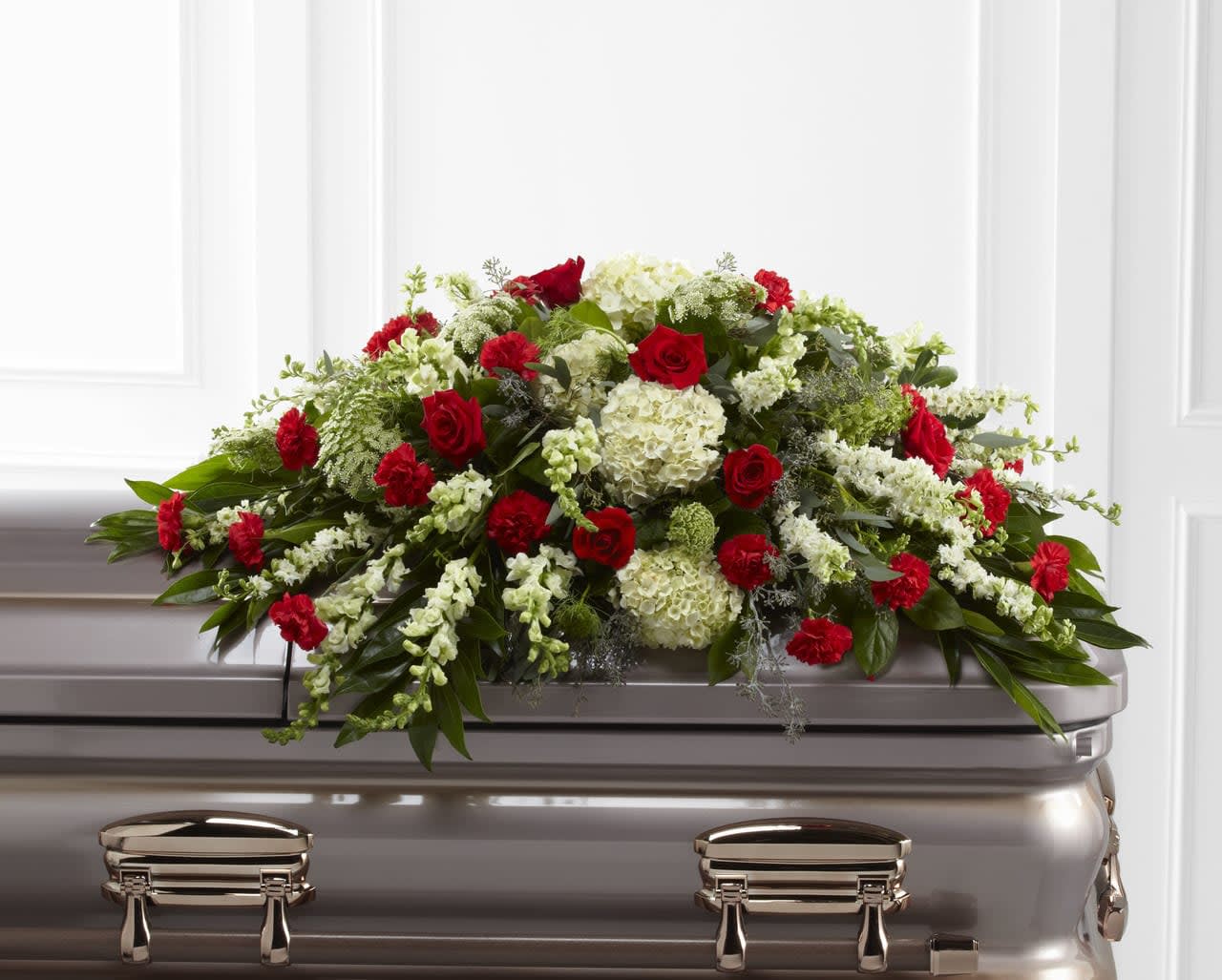 Red and white floral casket spray with roses and hydrangeas on a silver casket