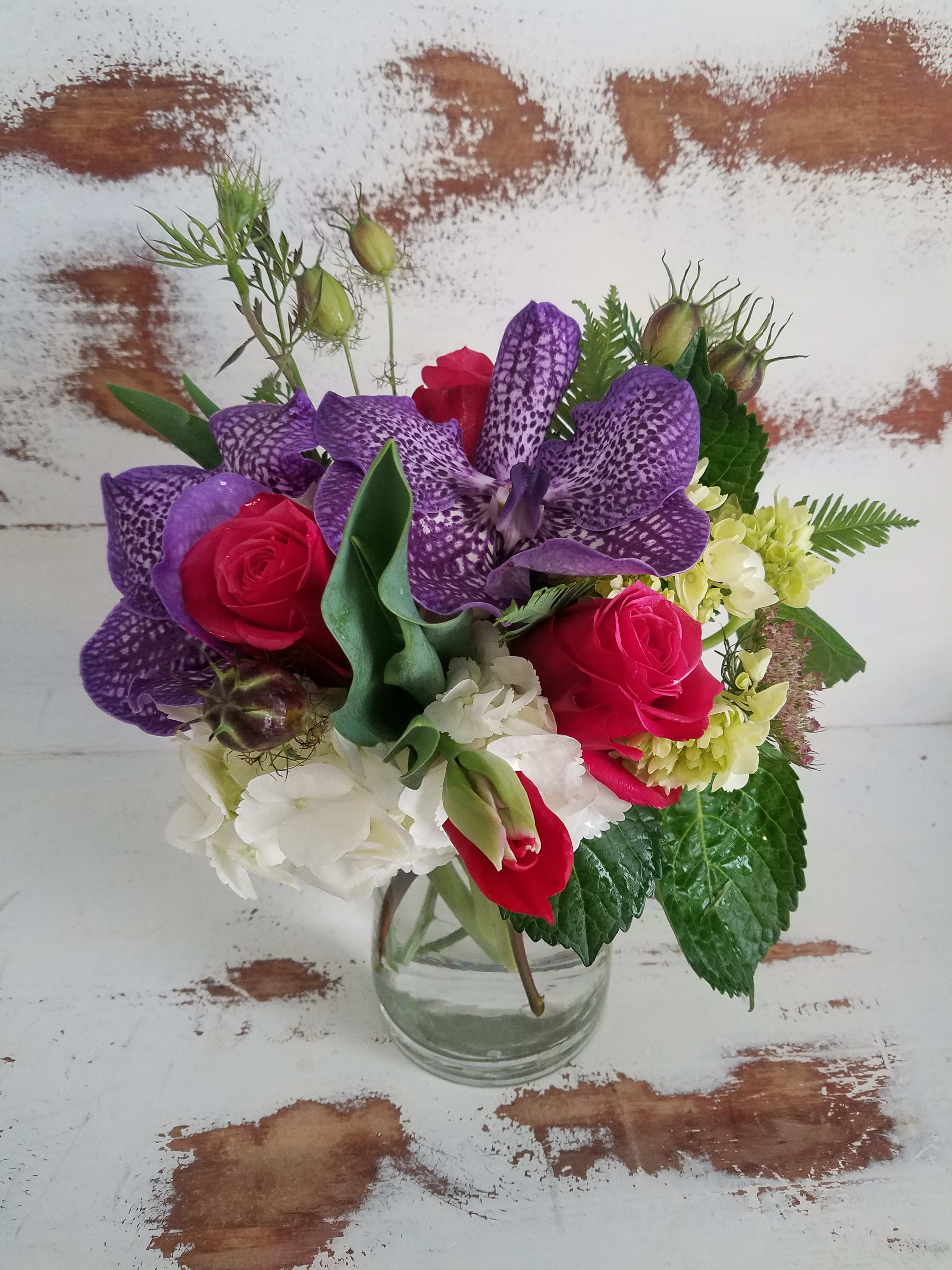 Bouquet of purple orchids, red roses, and white hydrangea in a clear glass vase