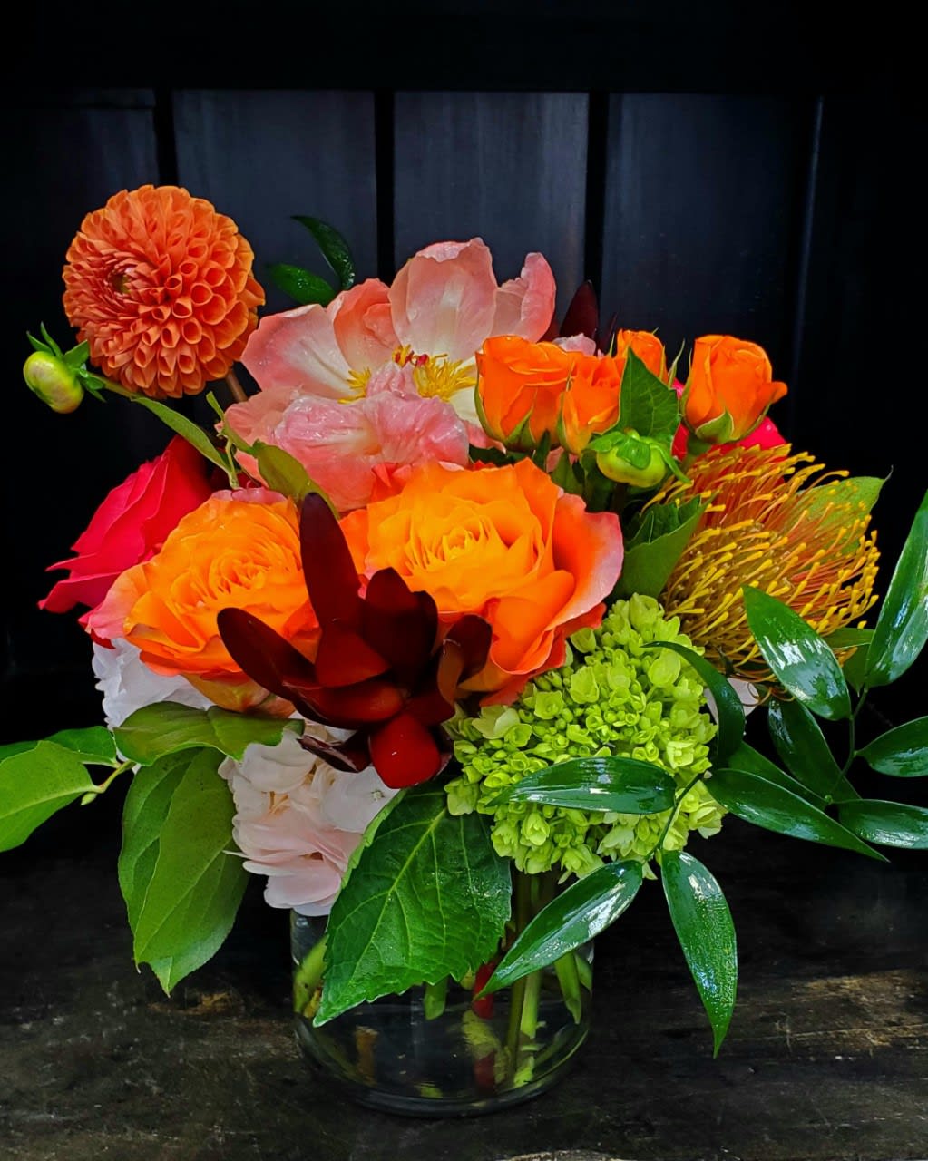Bright mixed bouquet of orange, pink, and green flowers in a glass vase