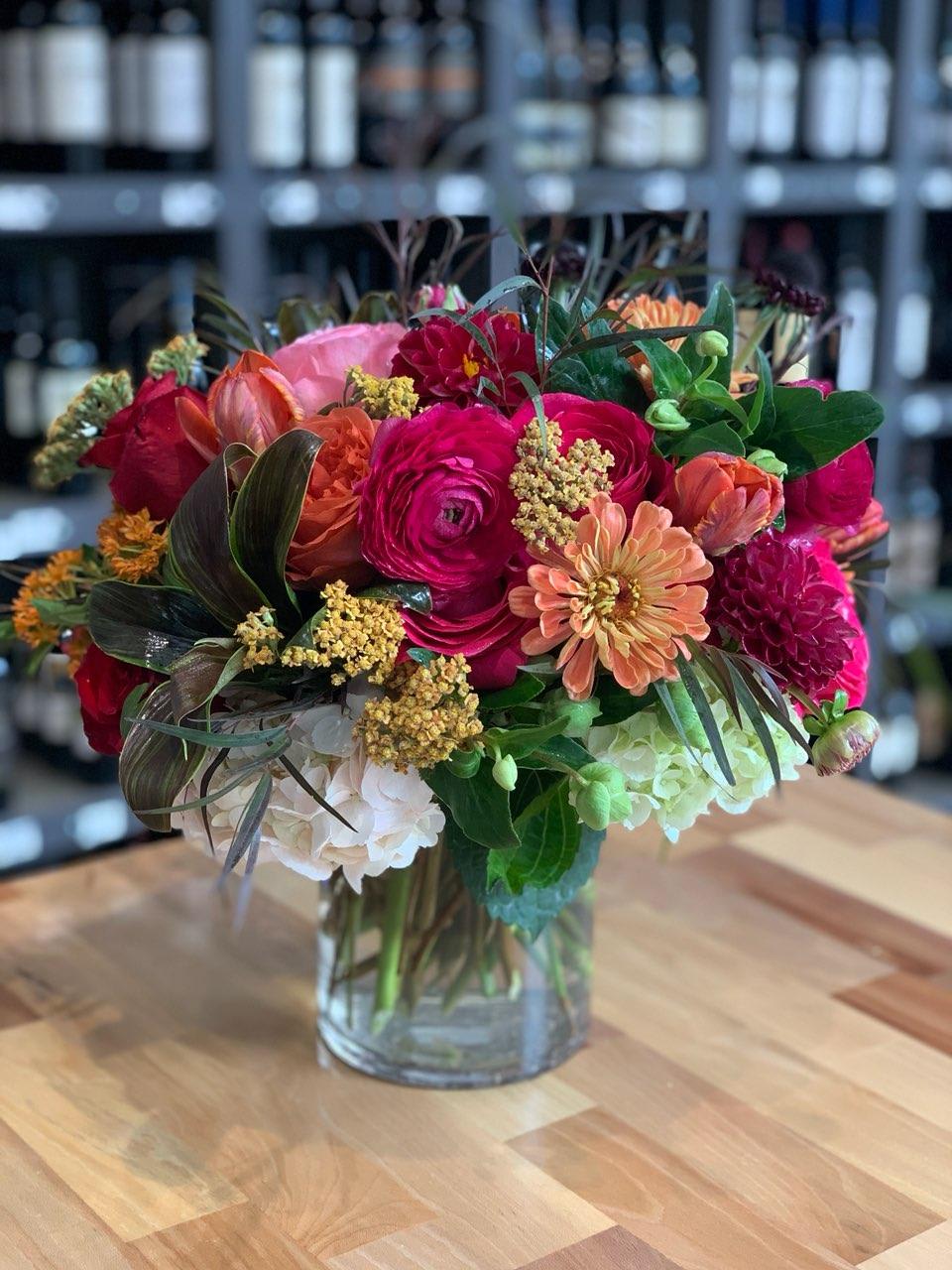 Mixed bouquet of pink, orange, red, and white flowers in a clear glass vase