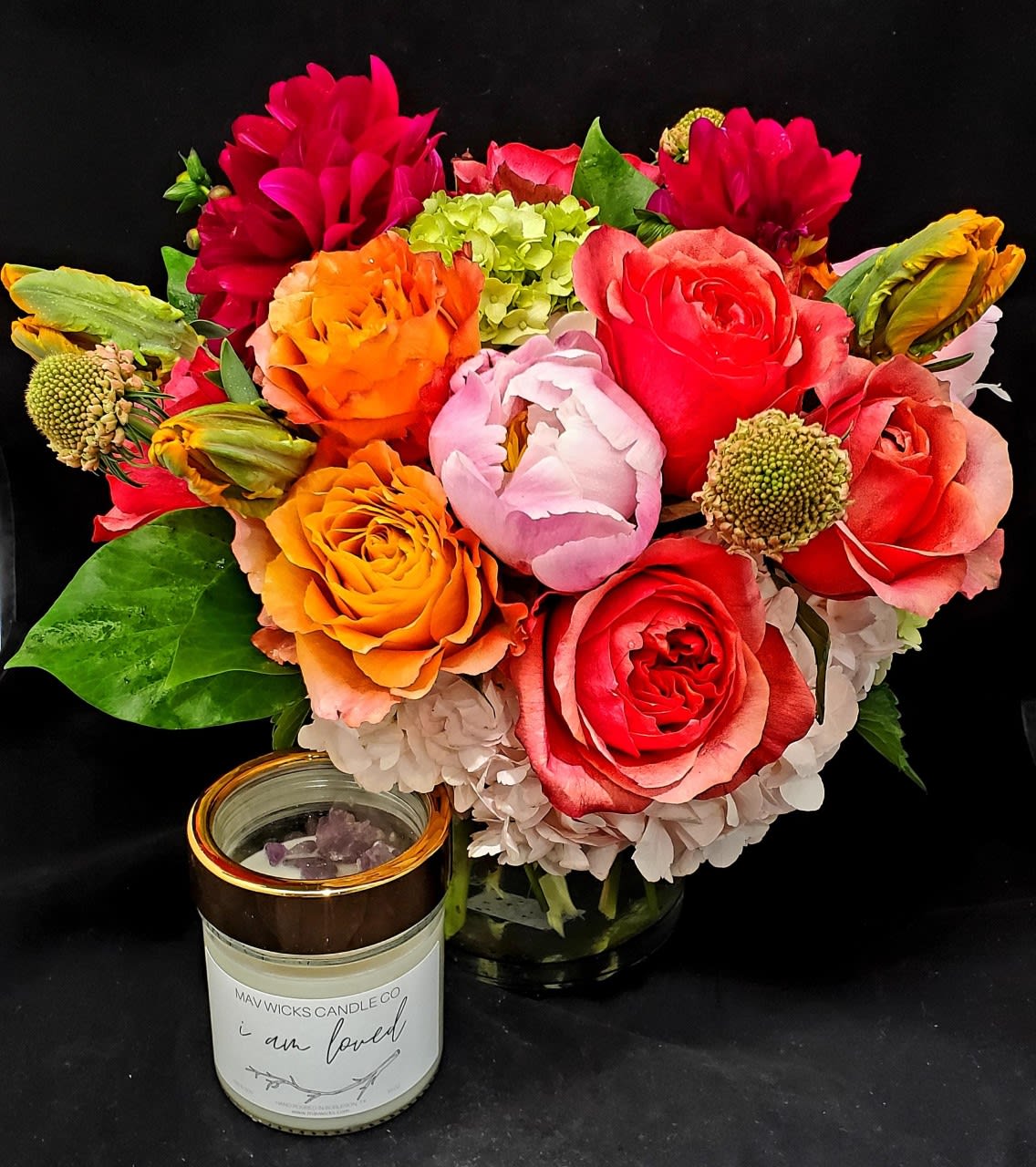 Bright mixed bouquet with roses, peonies, and hydrangeas beside a candle