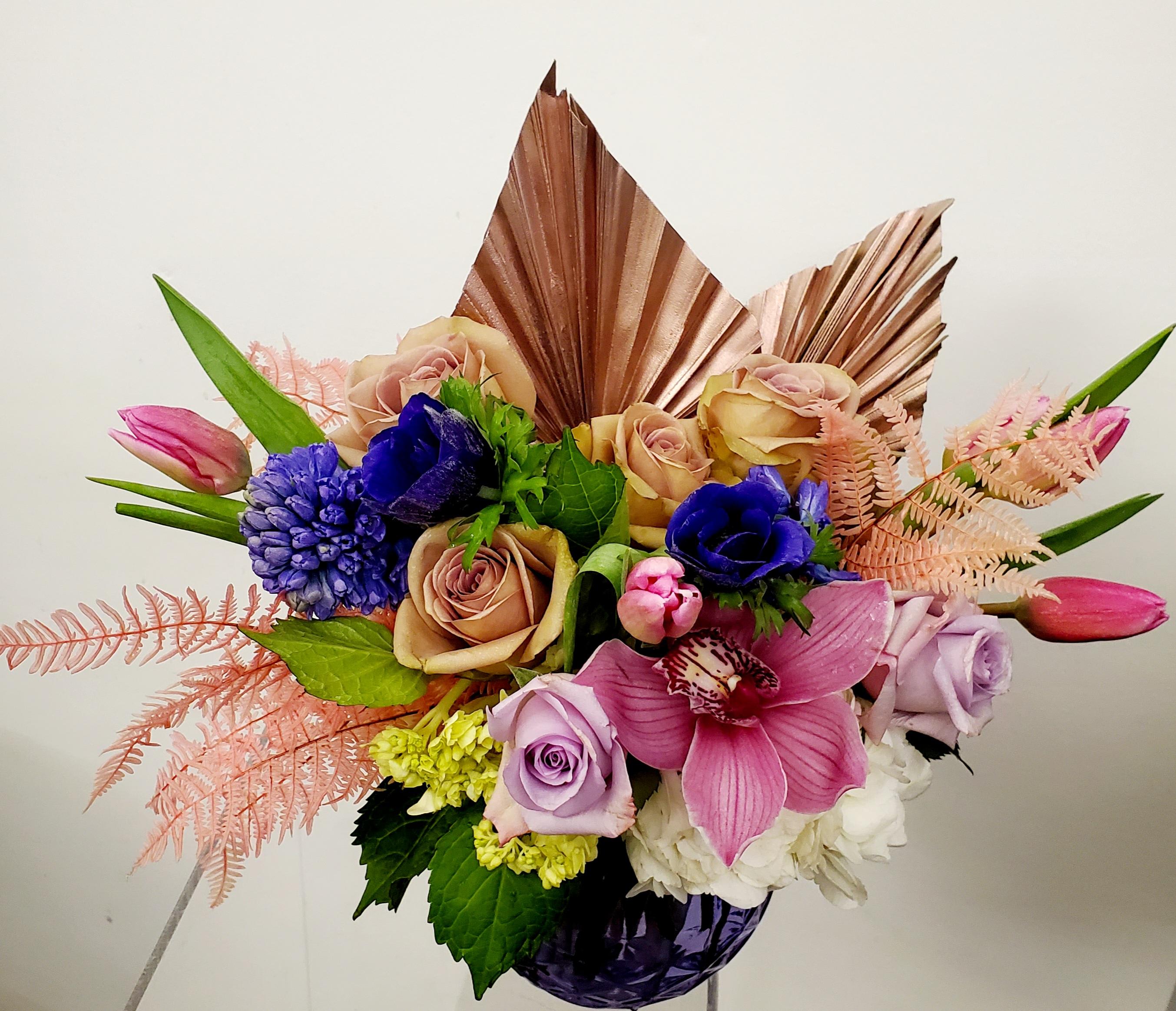 Bouquet of roses, orchids, and blue blooms in a purple vase