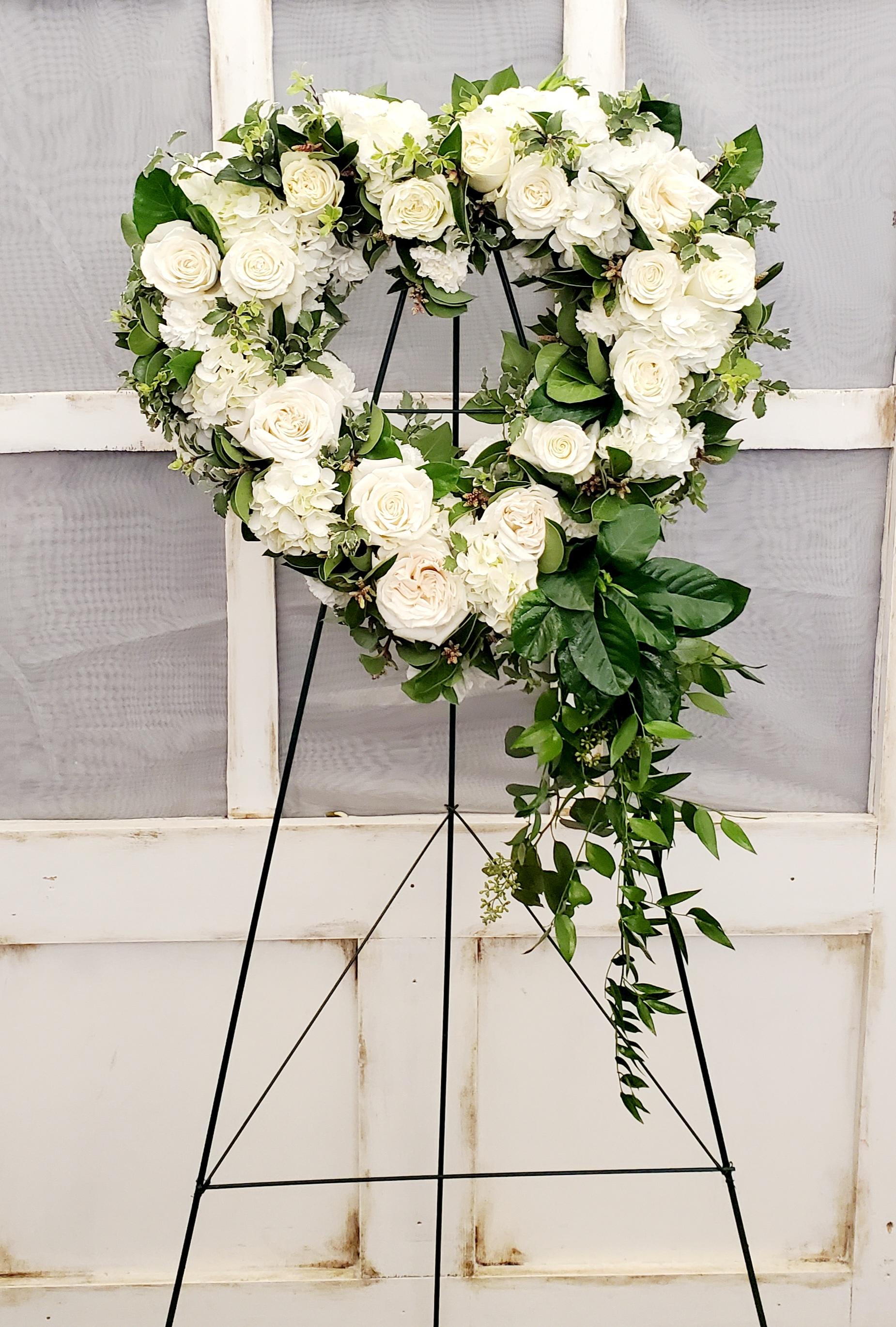 Heart-shaped white rose wreath on a black stand with trailing greenery