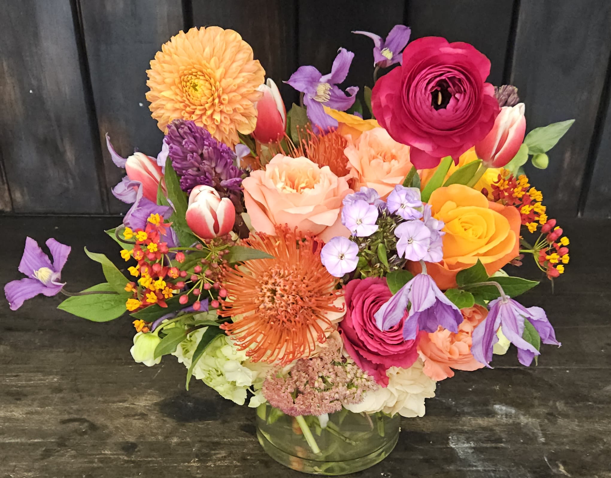 Colorful mixed bouquet in a clear glass vase with roses, tulips, and dahlias