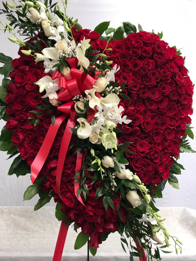 Heart-shaped red rose arrangement with white flowers and a red ribbon