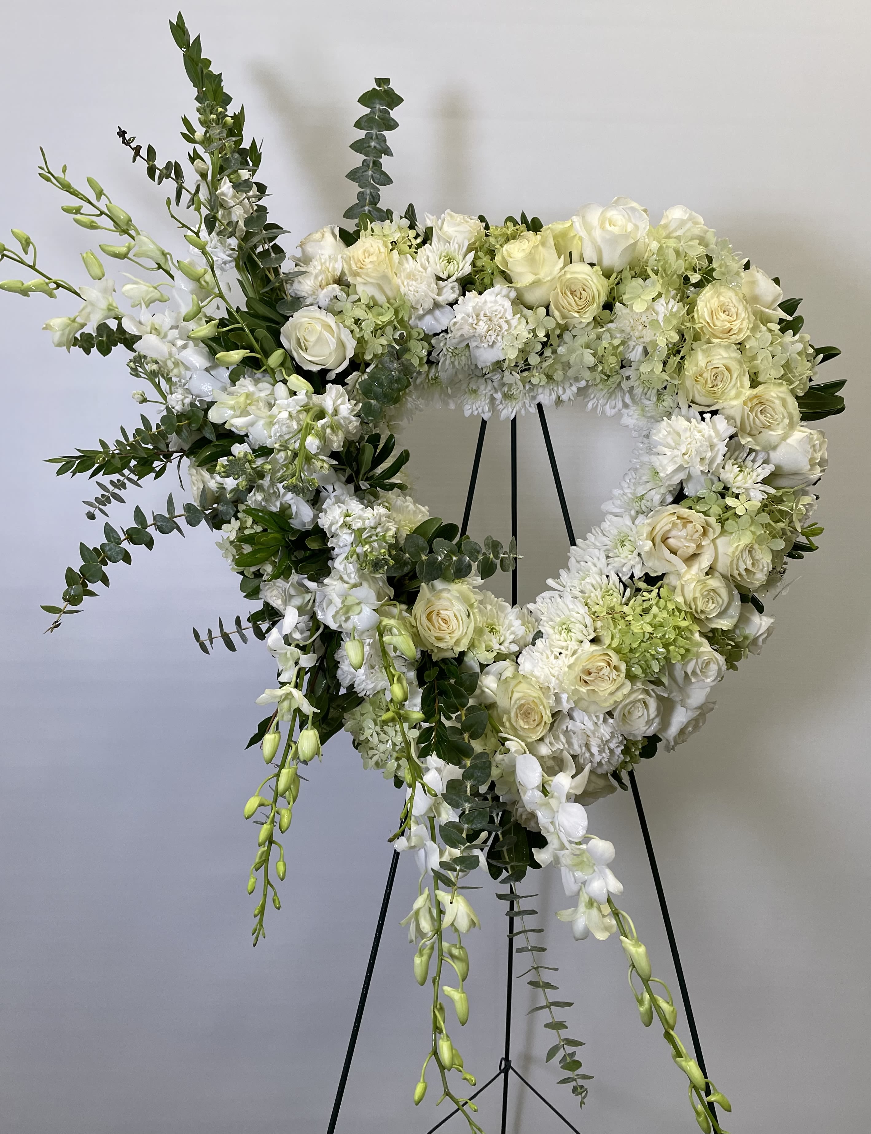 Heart-shaped white floral wreath on a black stand