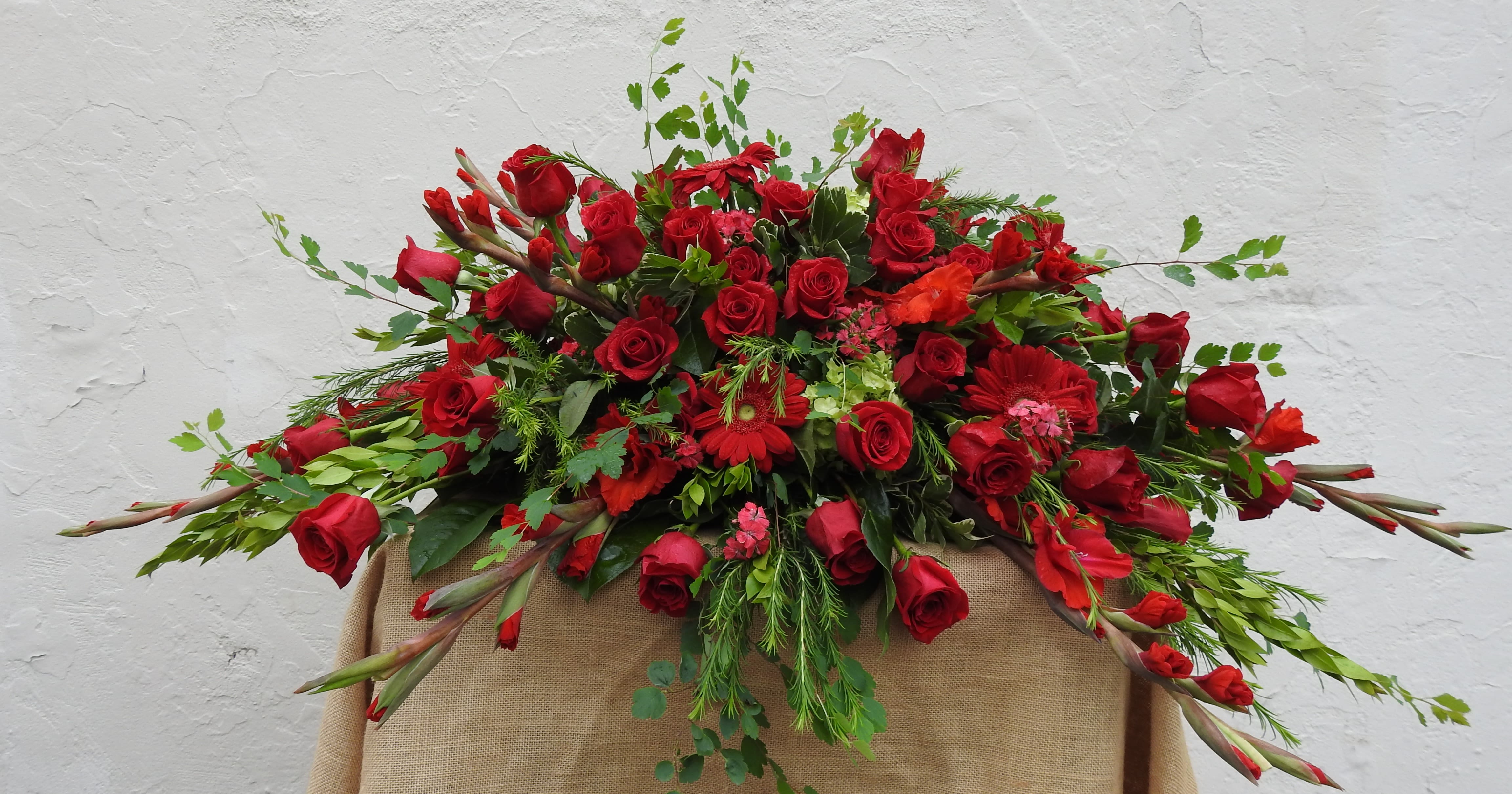 Large red rose arrangement with mixed greenery on a burlap-draped stand