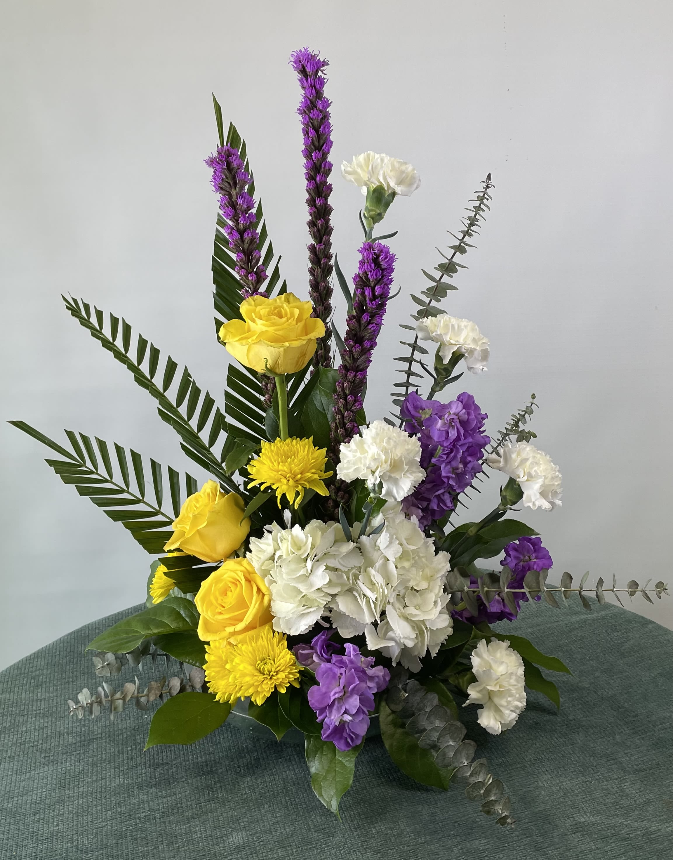 Yellow roses, white carnations, and purple flowers in a tall arrangement
