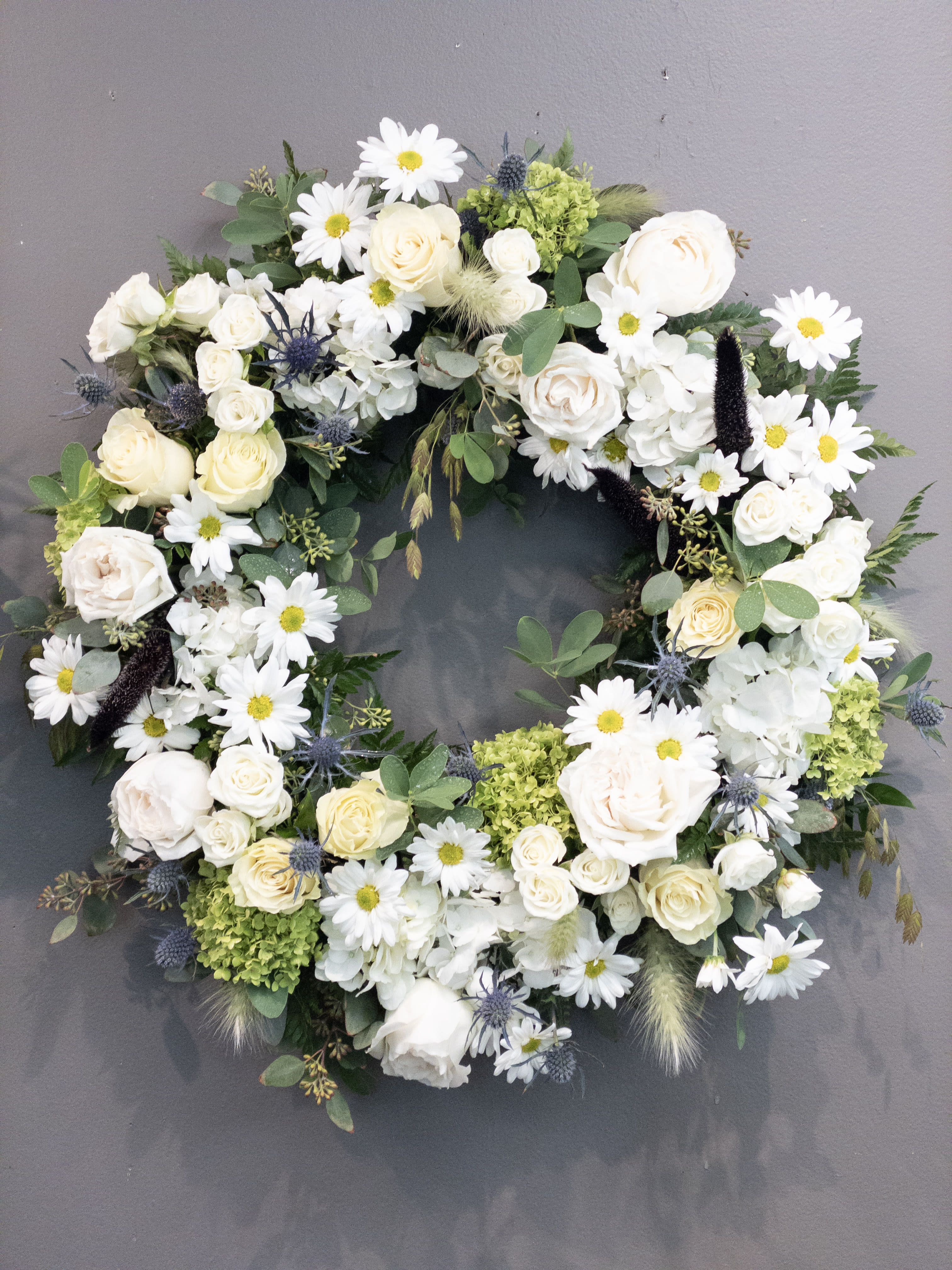 White and cream floral wreath with roses, daisies, and hydrangeas on a gray background