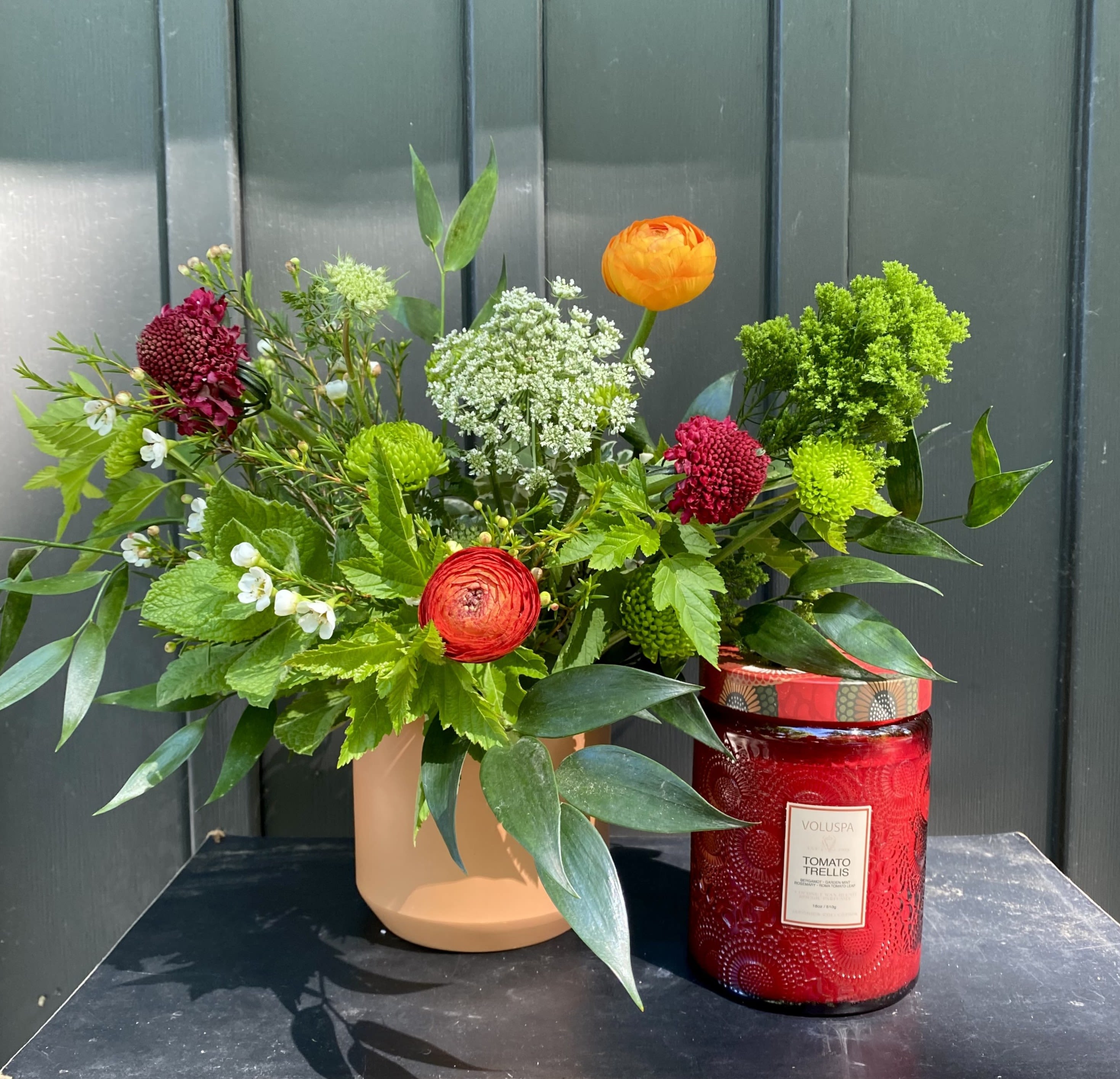 Tomato Gift Set - A fresh tomato inspired arrangement paired with our large Voluspa tomato trellis glass jar candle. Arrangement measures approximately 10" x 10". Candle is 18 oz, fragrance notes include: Bergamot, Garden mint, Rosemary and Roma tomato leaf. Upgrade to deluxe or premium for additional luxe blooms in the arrangement.