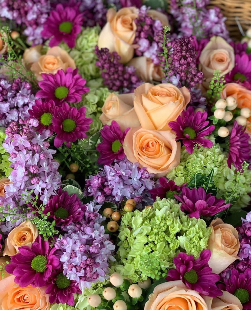 Peach roses with purple daisies and lilac blooms in a dense floral arrangement