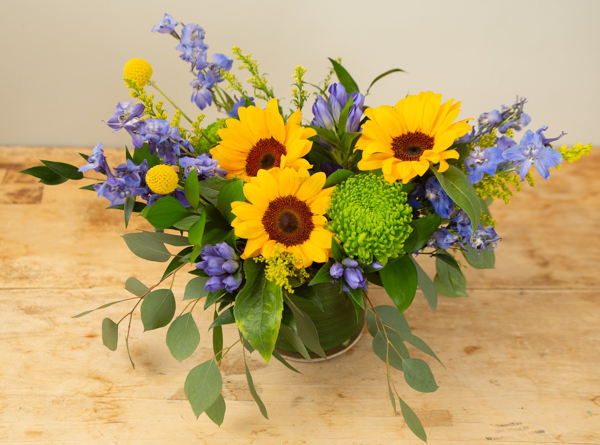 Sunflowers and blue flowers arranged in a low vase