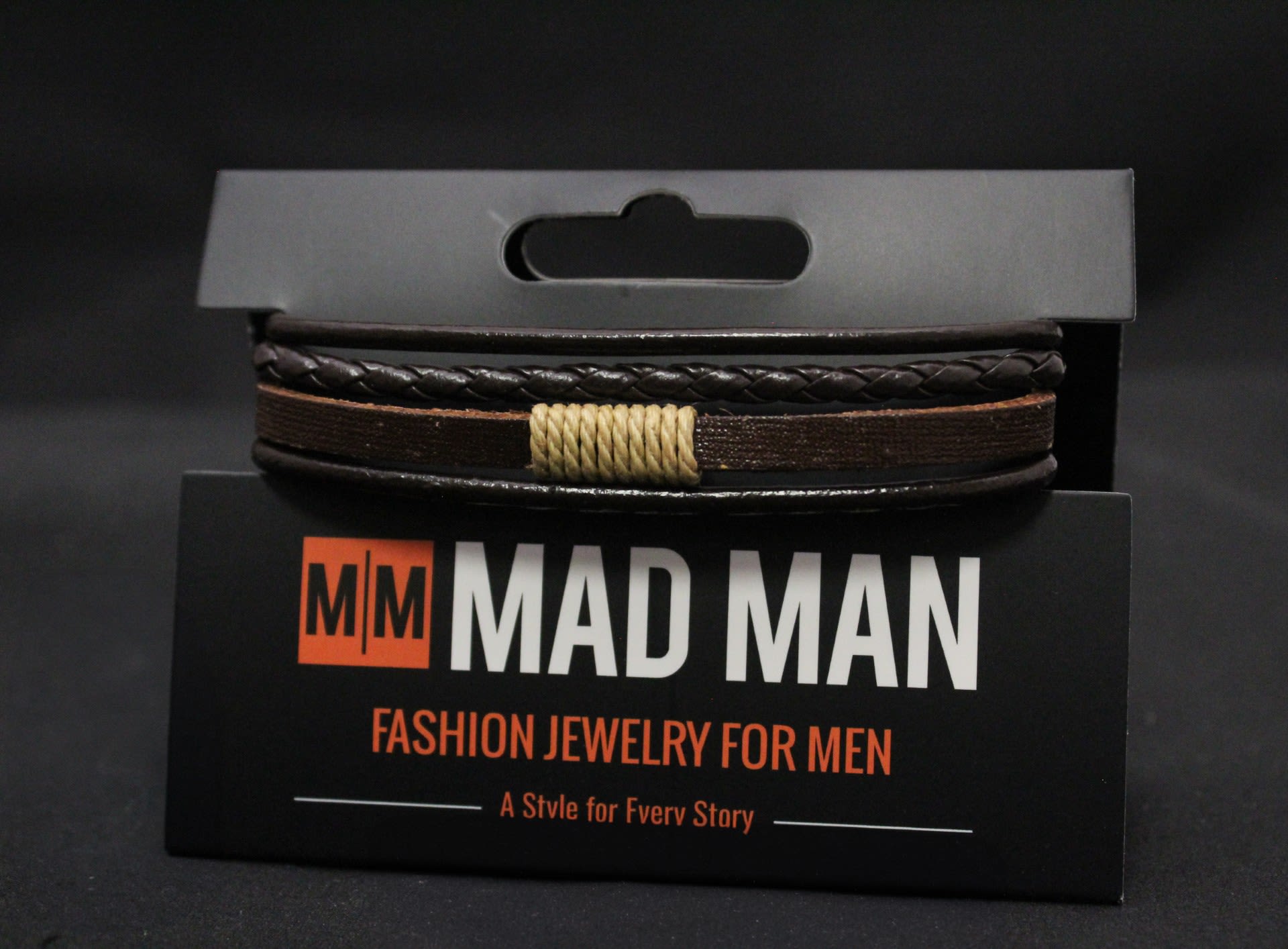Men's Mad Man Leather Bracelet - Ridgeland - Handcrafted leather and braided cord combine for a rugged, casual accessory perfect as a small gift or stocking stuffer for him - a men's bracelet ideal for birthdays, Father's Day, or "just because" moments. The layered cuff-style arrangement reads dark and masculine, designed to make the person you're gifting feel effortlessly put together without trying too hard.  Multiple slim bands in deep brown and black are woven together with a braided top strand and a contrasting light tan wrapped accent at the center, creating visual texture and a warm pop against the darker leathers. The adjustable tie closure keeps the fit flexible, and the bracelet is presented on a sleek black.  This is the sort of everyday piece he'll reach for with jeans or a leather jacket - rustic, understated, and wearable. Size adjusts via the cord ties.