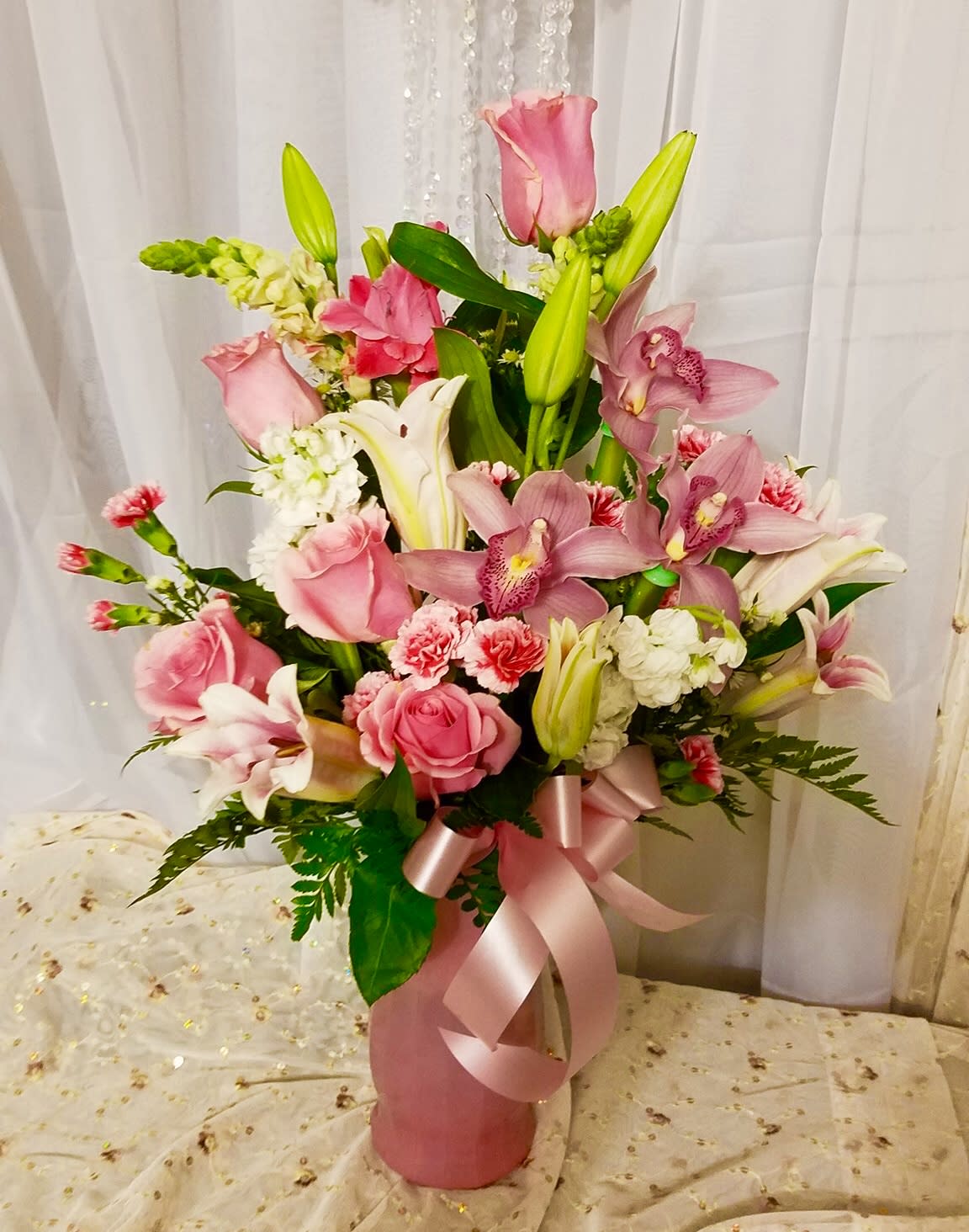 Pink and white floral arrangement in a pink vase with a ribbon bow