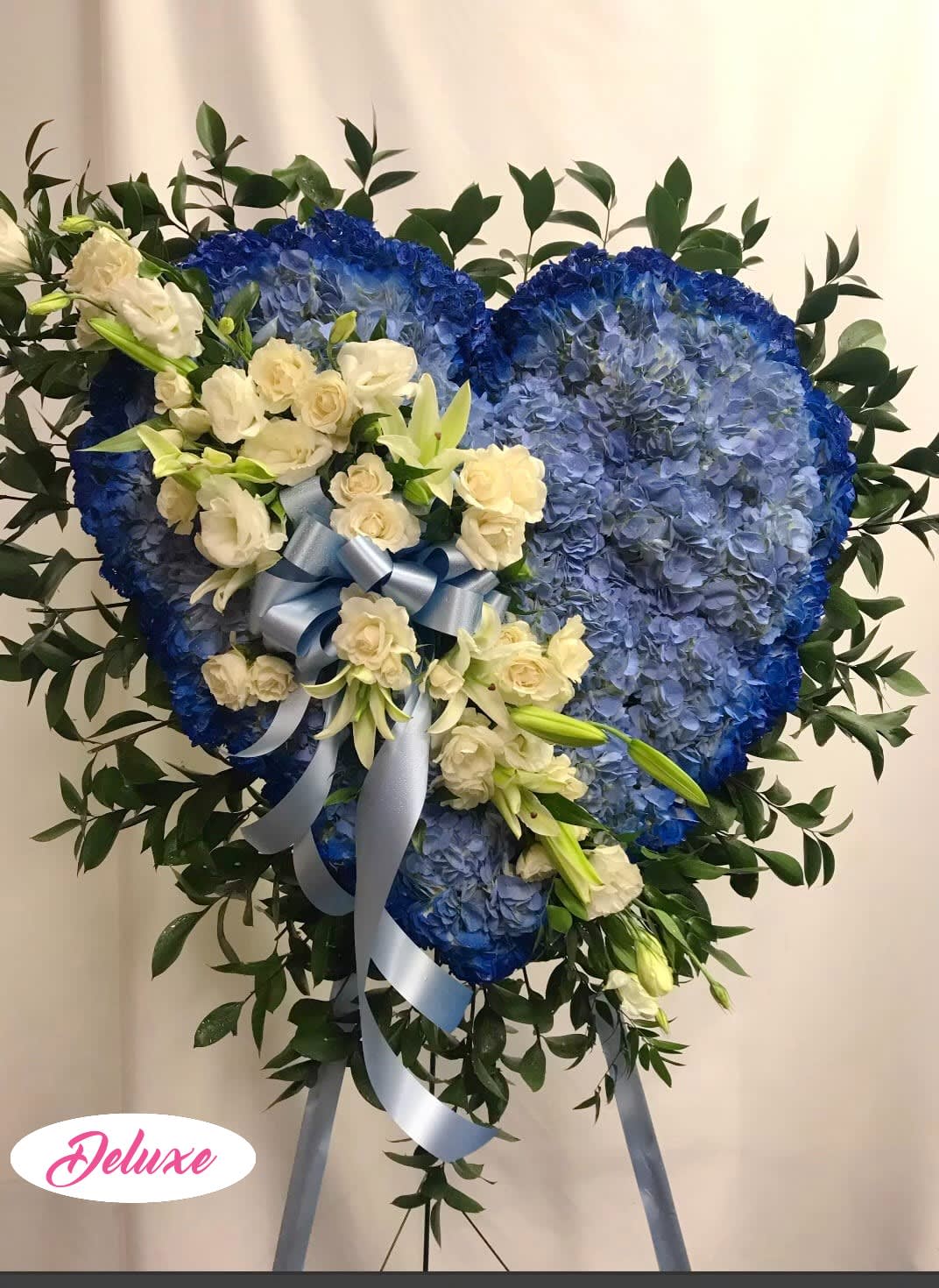 Heart-shaped blue floral tribute with white roses and lilies