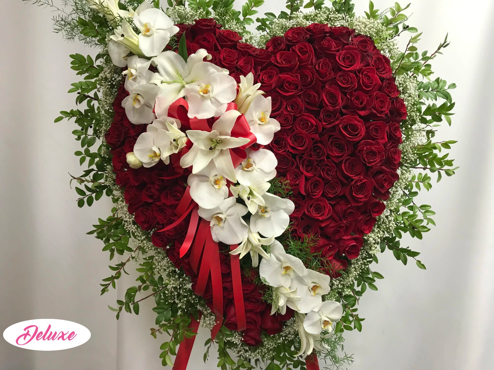 Heart-shaped red rose arrangement with white orchids and a red ribbon