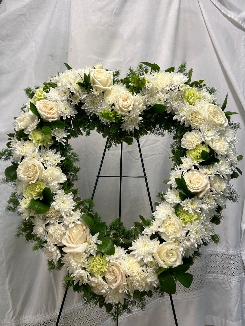 Heart-shaped white floral wreath on a black stand