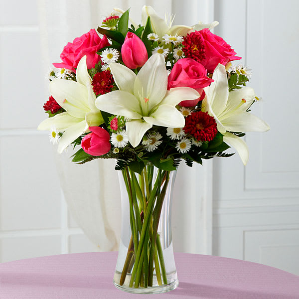 Spring Samba  - Brilliant fuchsia roses, hot pink tulips, hot pink matsumoto asters, white Asiatic Lilies, white monte casino asters, and lush greens are seated in a clear glass vase.
