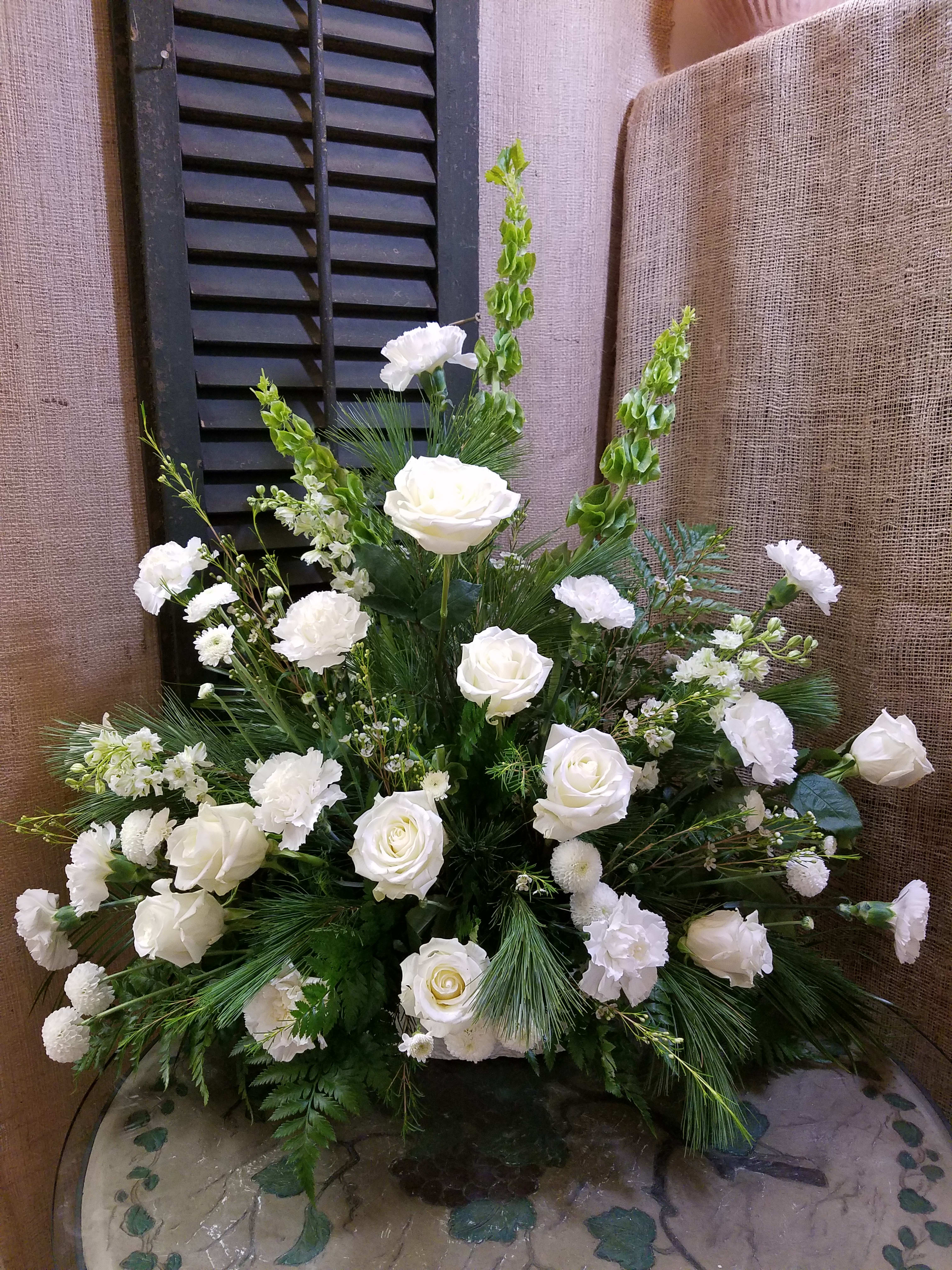 White roses and carnations arranged in a large vase with greenery