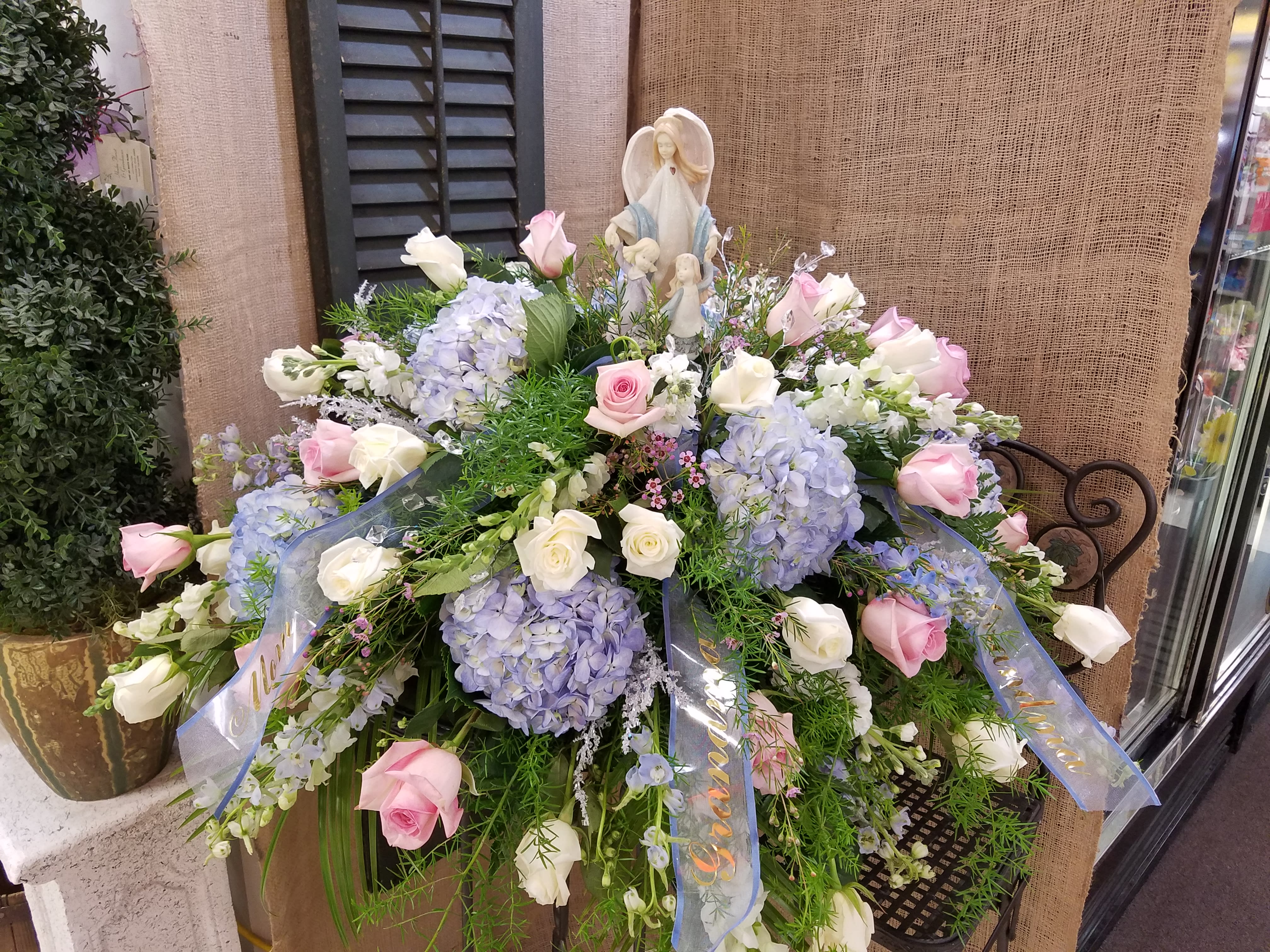 Large pastel floral spray with roses and hydrangeas around a religious figurine