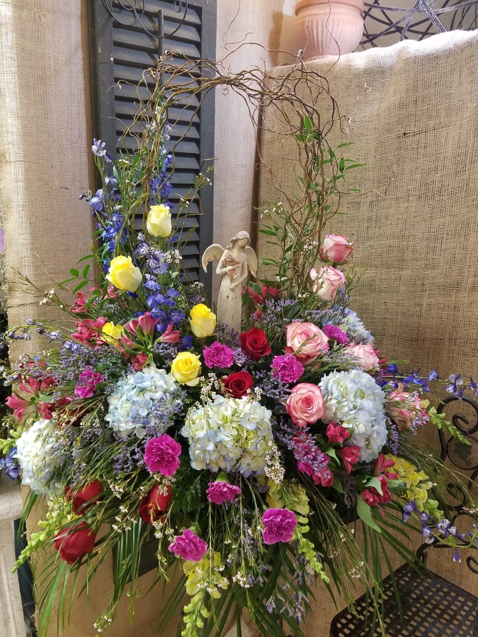 Large mixed floral arrangement with roses, hydrangeas, and an angel figurine