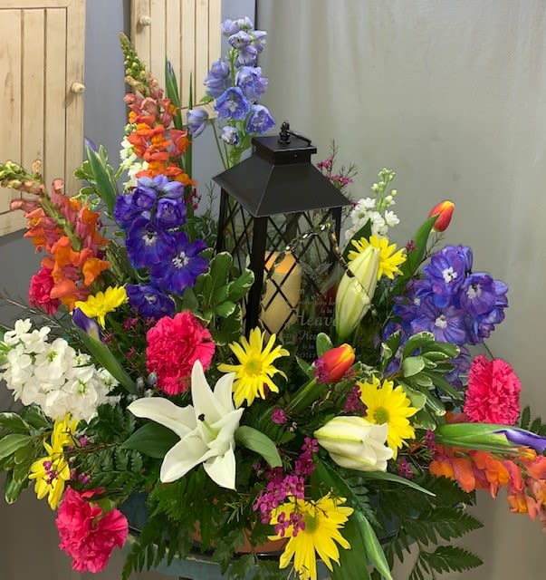 Colorful floral arrangement with lilies, daisies, and snapdragons around a black lantern