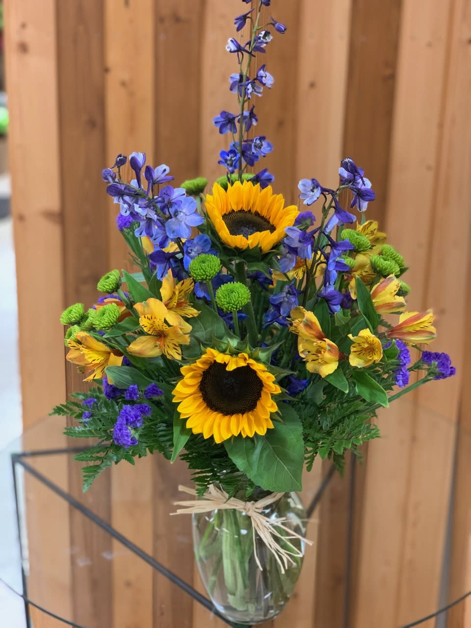 Bouquet of sunflowers, blue flowers, and yellow alstroemeria in a glass vase