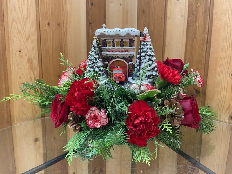 Christmas floral arrangement with red roses and carnations around a small snowy building