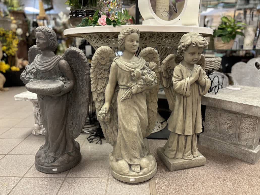 Three angel statues displayed in a store, with a small floral arrangement on a table behind them.