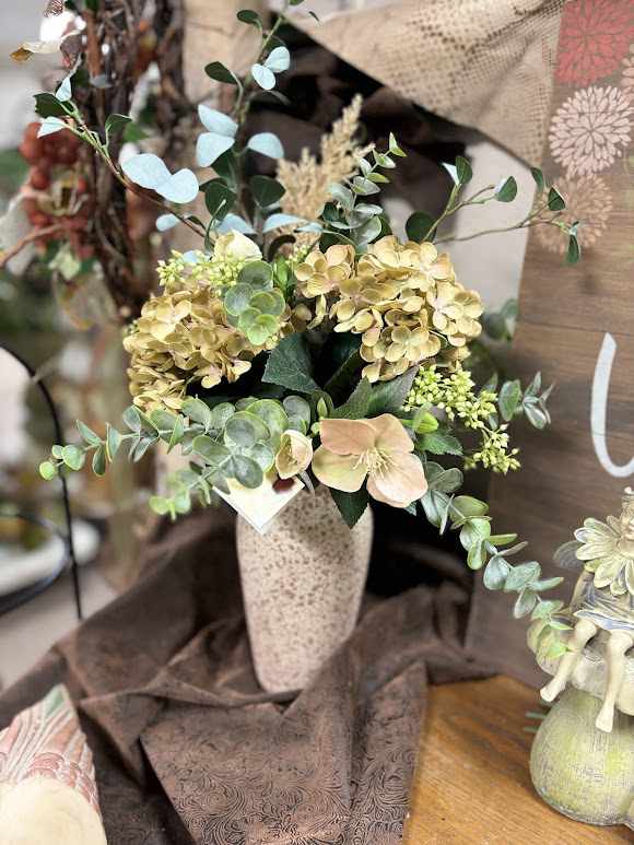 Arrangement of pale hydrangeas and greenery in a tall vase