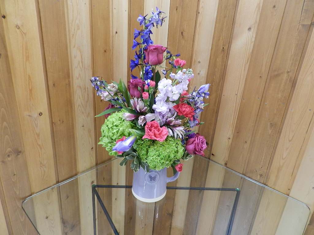 Mixed bouquet in a lavender pitcher vase with pink, purple, and green blooms