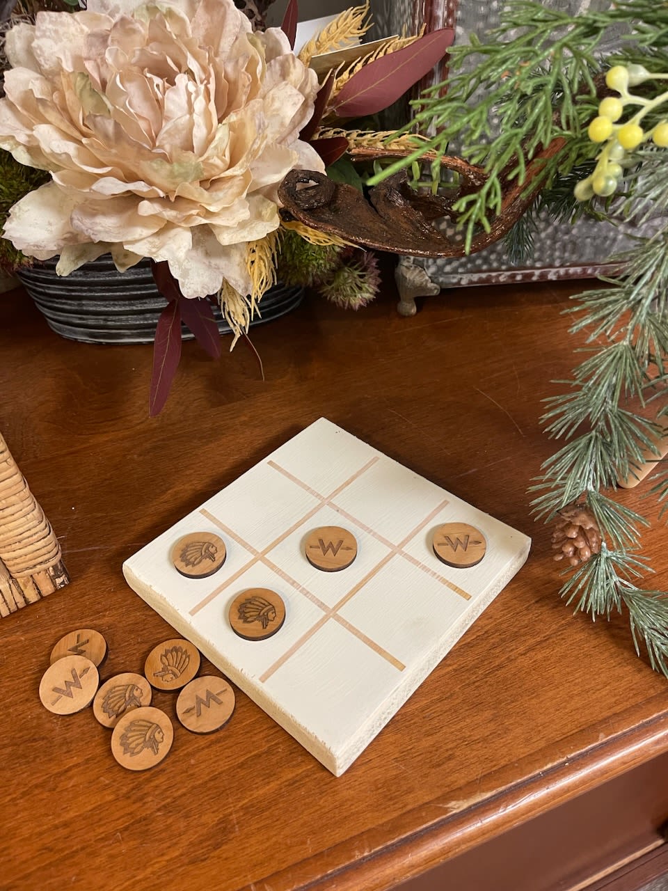 Tic-tac-toe board with wooden game pieces on a table beside a floral arrangement