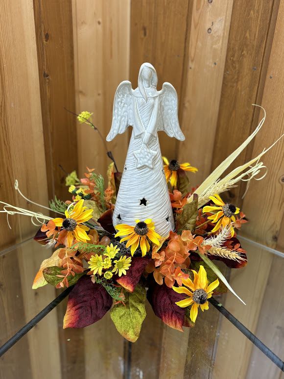 Angel figurine surrounded by yellow and orange flowers in an autumn arrangement