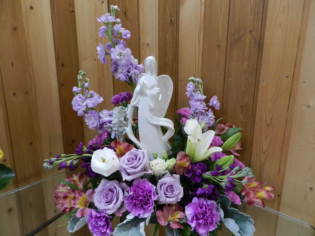 Purple and white floral arrangement with an angel figurine