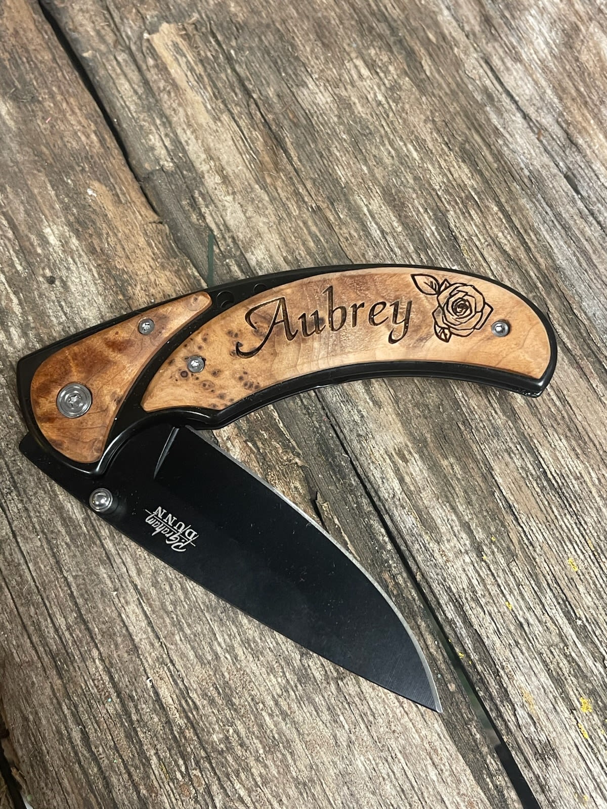 Engraved folding knife with a wooden handle and black blade