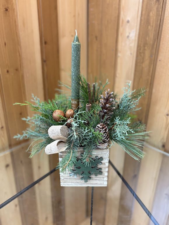 Small evergreen candle arrangement in a wooden box with pinecones and a teal taper candle