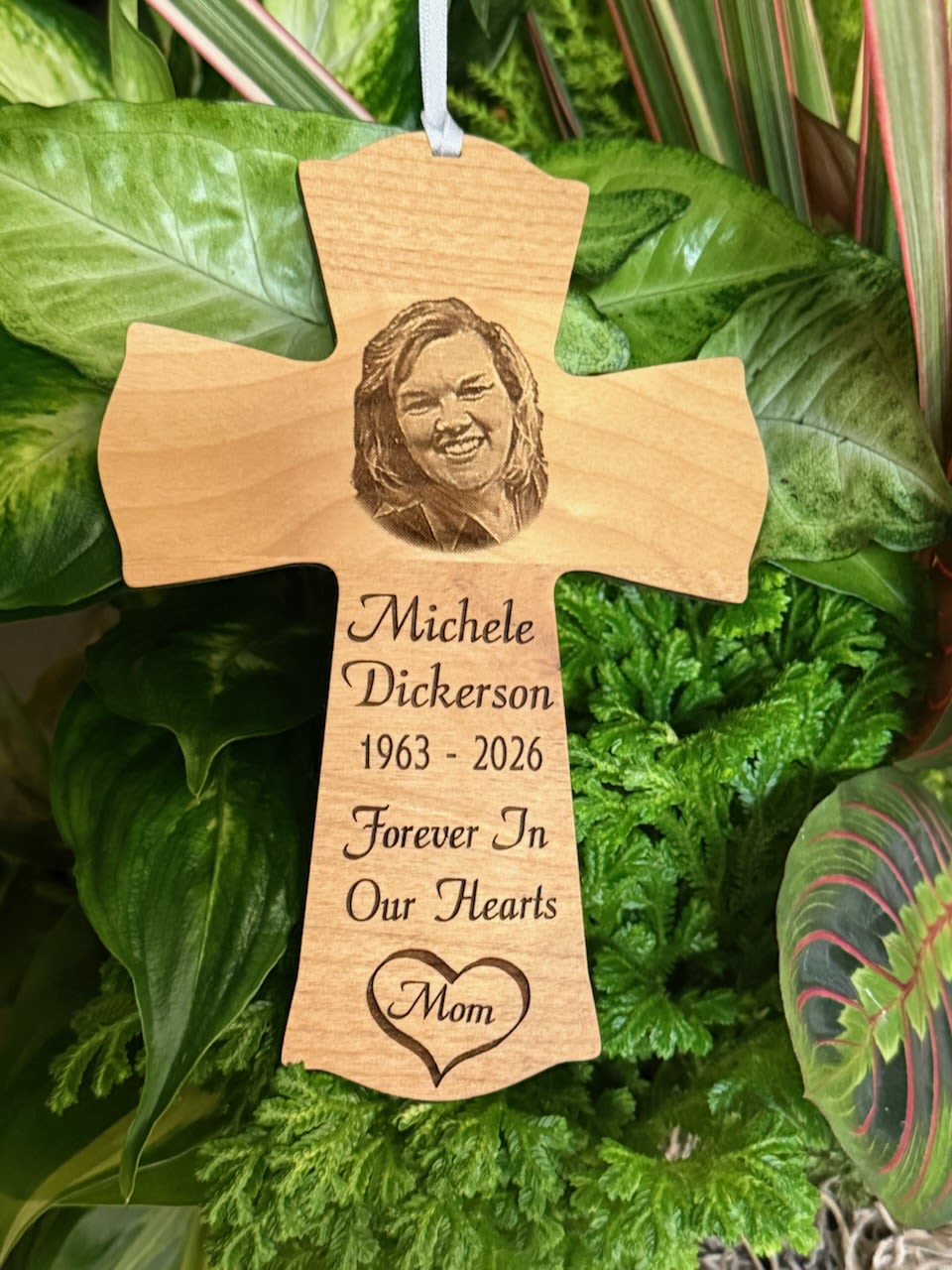 Wooden memorial cross with engraved portrait and text among green foliage