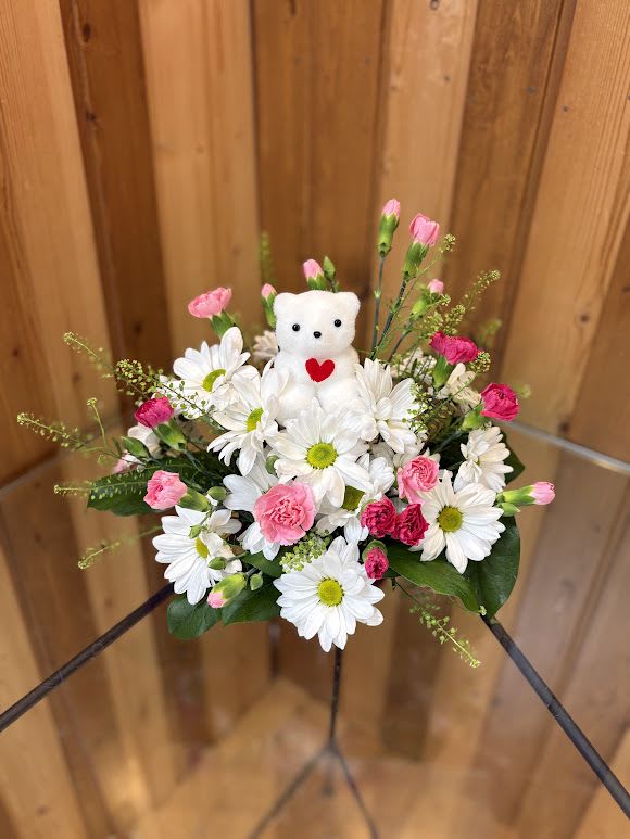 White daisies and pink carnations with a small teddy bear centerpiece