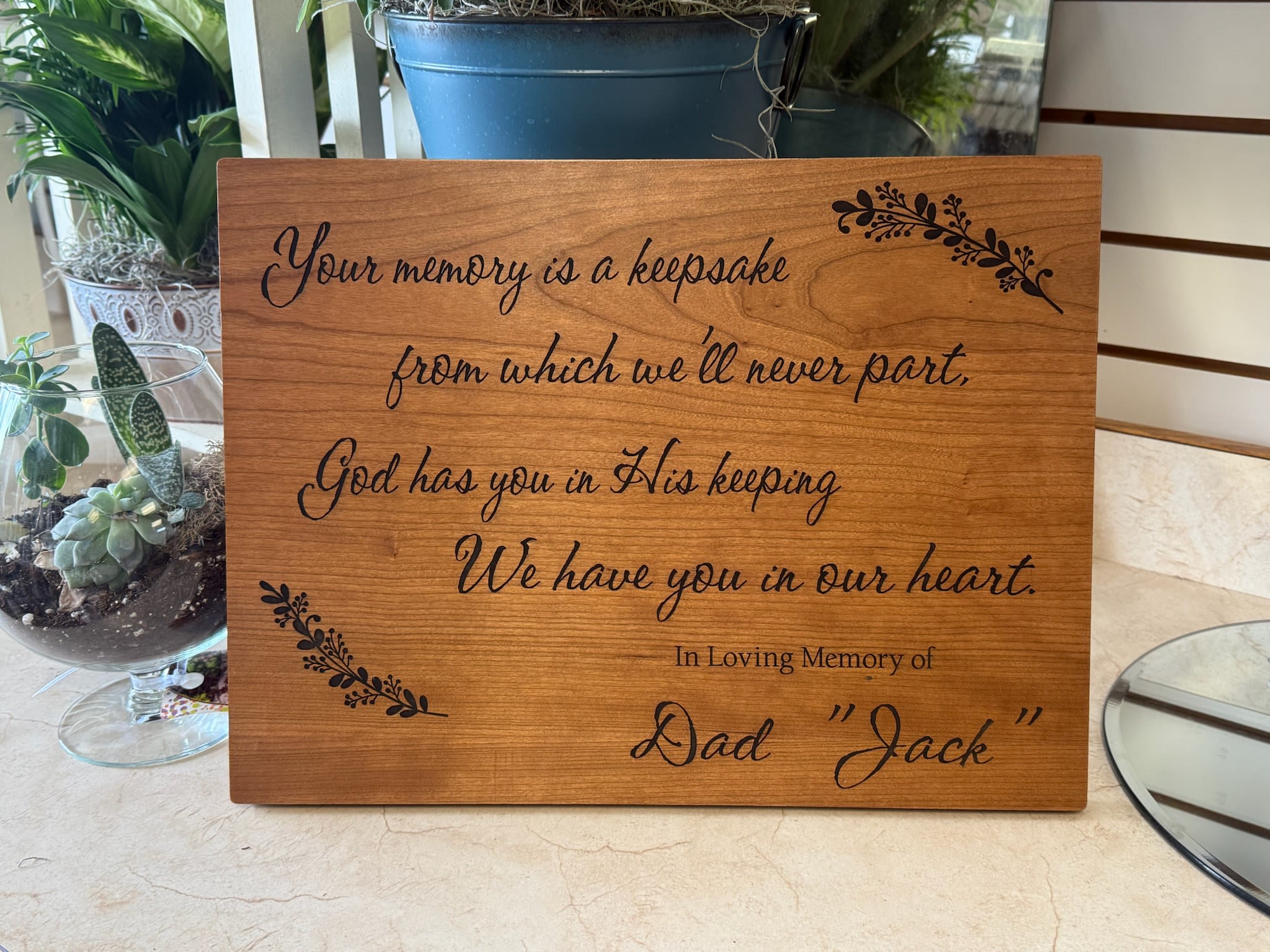 Wood memorial plaque with engraved sympathy message and potted plants nearby