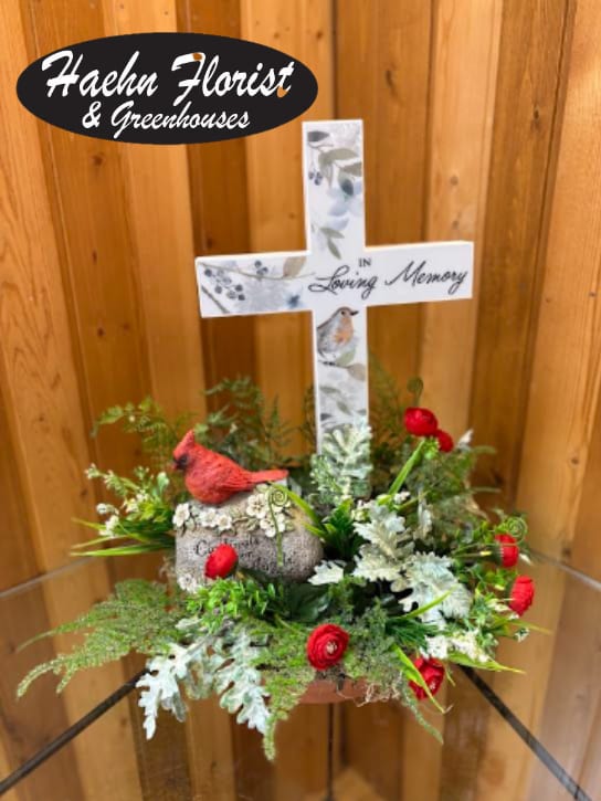 Memorial cross arrangement with red flowers and a bird figurine