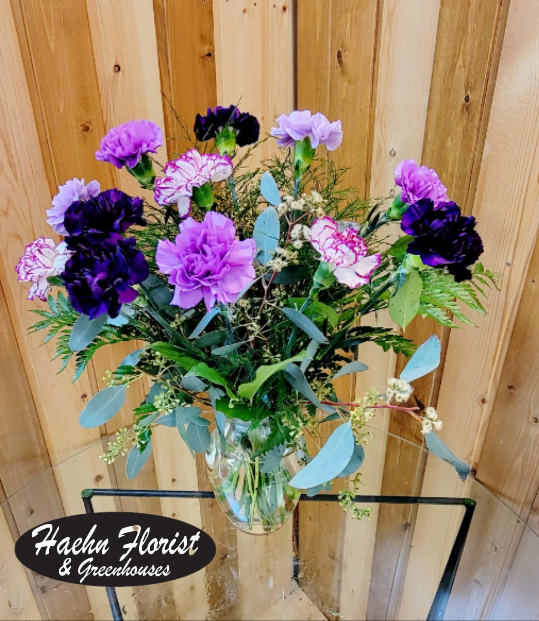 Carnation Simplicity - A lively mix of deep purple, lavender and white carnations makes a cheerful birthday bouquet that also feels perfect for Get Well, New Baby, Thank You, or Just Because moments. The ruffled carnation blooms-including blossoms with delicate purple-edged petals-are spaced to showcase their texture and soft movement, giving the arrangement an airy, garden-fresh presence that will make the person you're thinking of feel genuinely celebrated.  Arranged in a clear glass vase, the display is lifted by eucalyptus and other textured green foliage that adds height and a slightly wild, natural silhouette. Size and vase proportions highlight each bloom without looking dense; the result reads as refined yet warm. We may substitute flowers of equal value and color if seasonal availability changes-every substitution is chosen to preserve the overall look and sentiment.  This arrangement is especially lovely in spring and summer but works year‑round for Women's Day, Best Friends Day, Admin Professionals' Week, or Breast Cancer Awareness Month gifts when purple tones are meaningful. Order from Haehn Florist, Greenhouses, &amp; Flower Delivery at 410 Hamilton Rd. Wapakoneta and follow us on Facebook: www.facebook.com/haehnflorist for updates and delivery options.