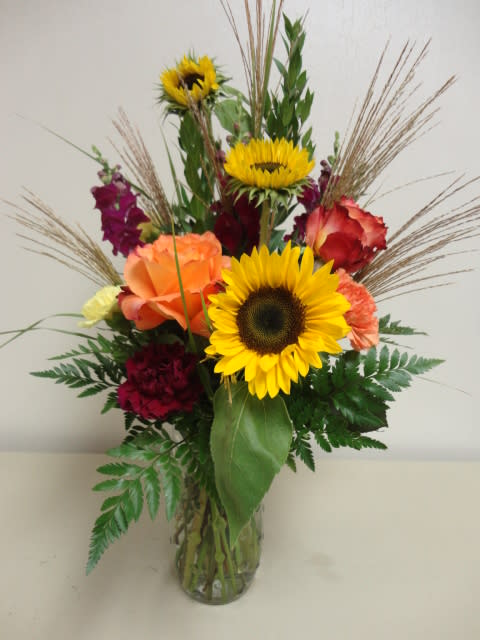 Mixed bouquet with sunflowers, roses, and carnations in a glass vase