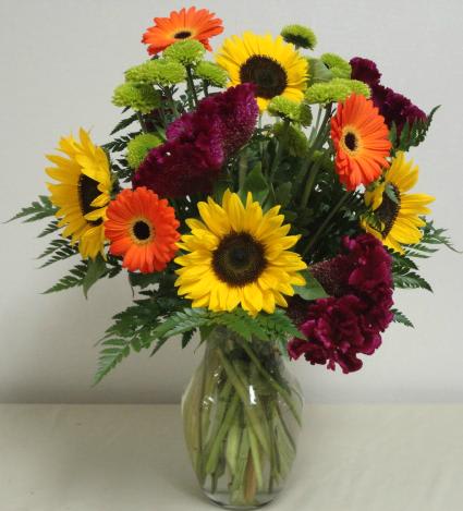 Bouquet of sunflowers, gerbera daisies, and burgundy flowers in a glass vase