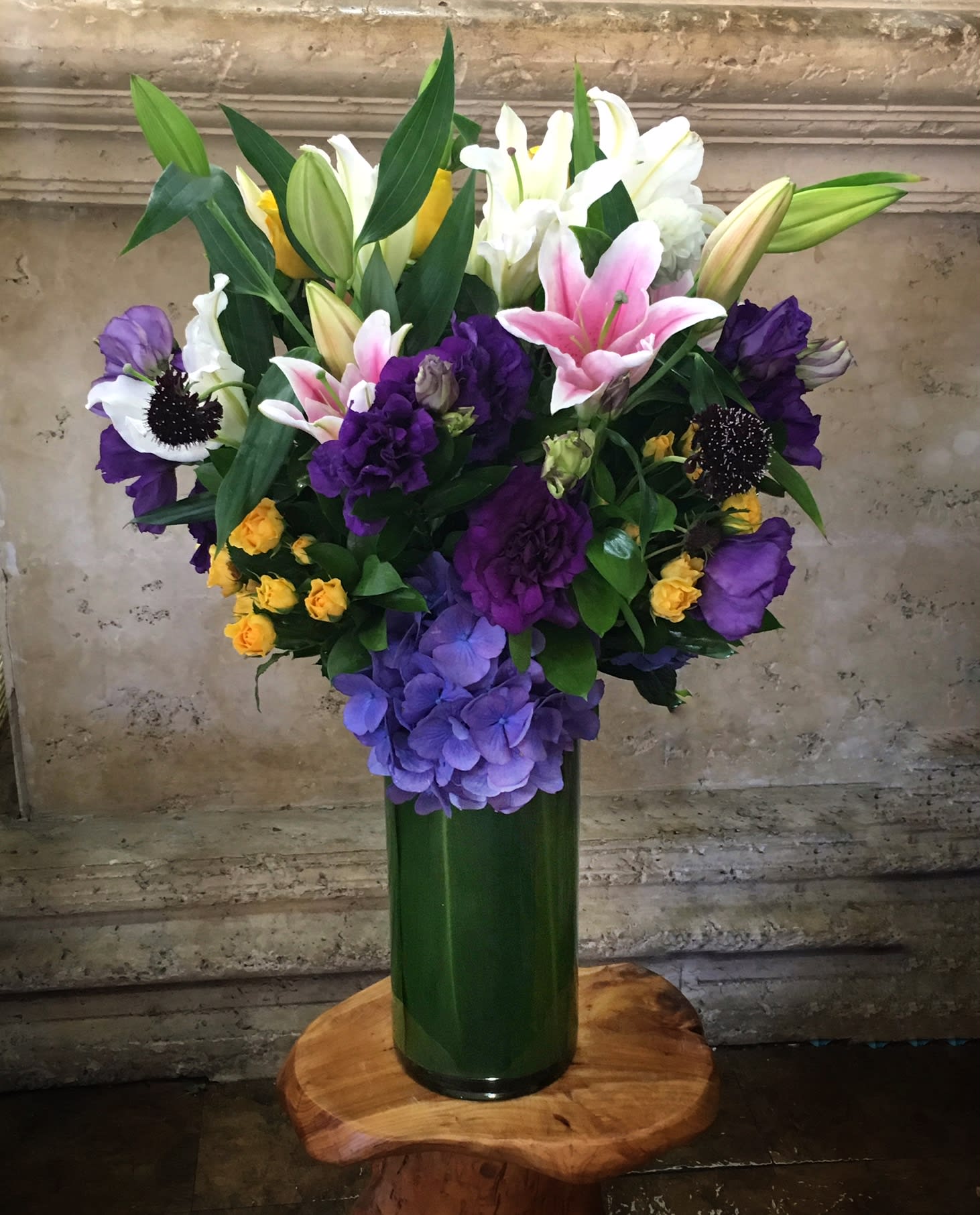 Mixed bouquet of lilies, roses, and hydrangeas in a tall green vase