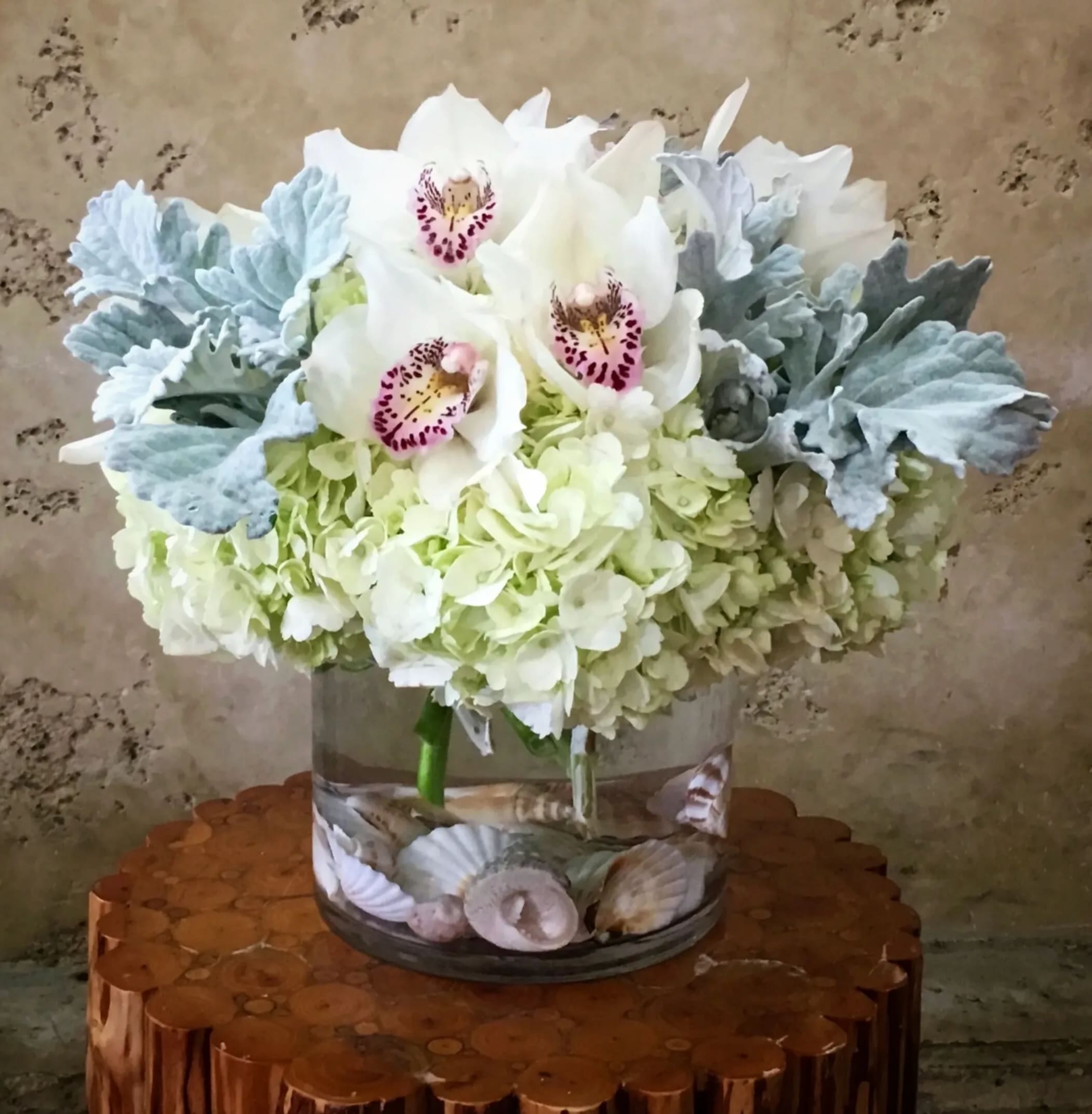 White orchids and pale hydrangeas in a glass vase with seashells