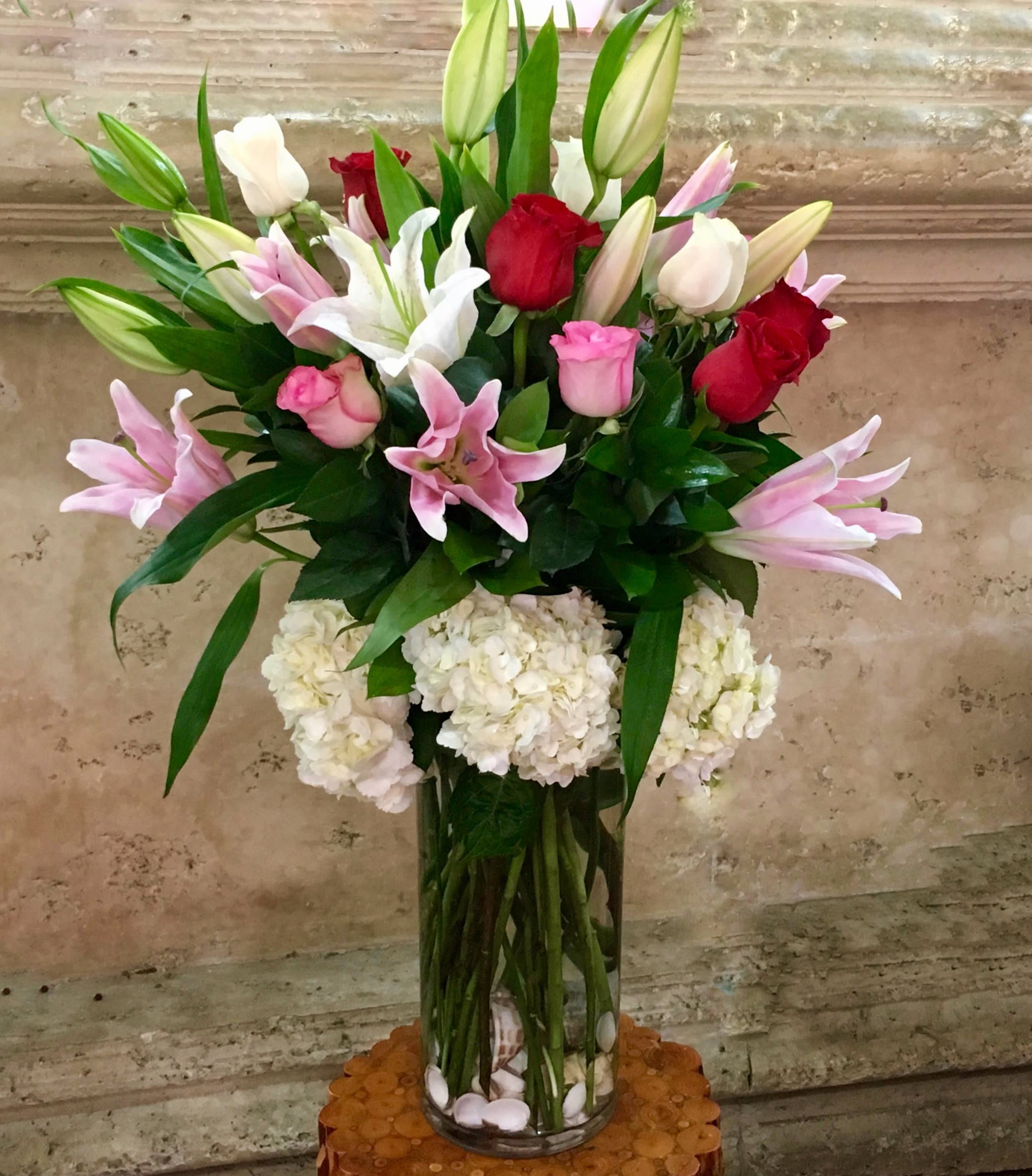 Tall bouquet of pink and red roses with lilies in a glass vase
