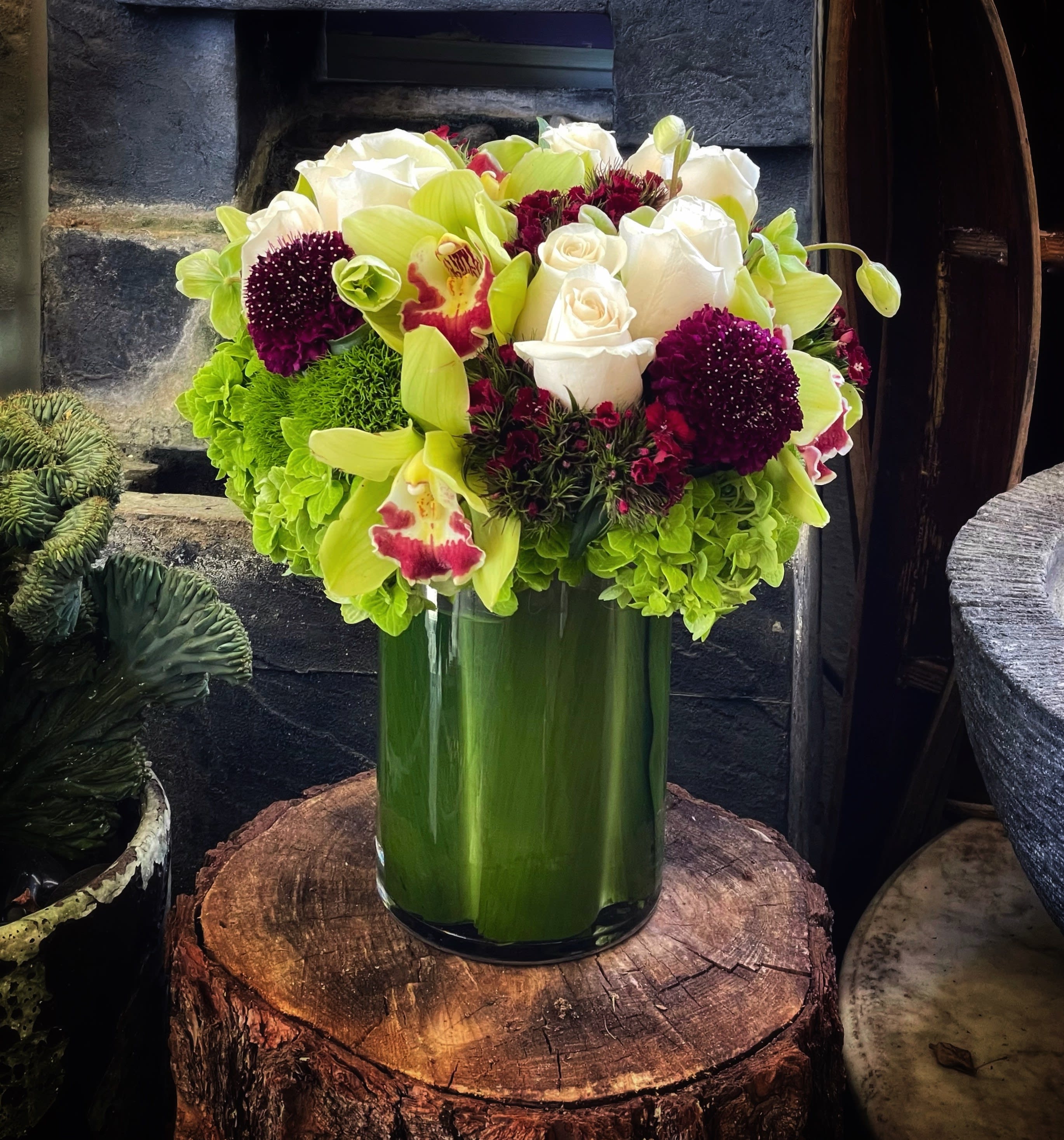 Bouquet of white roses, green orchids, and burgundy blooms in a glass vase