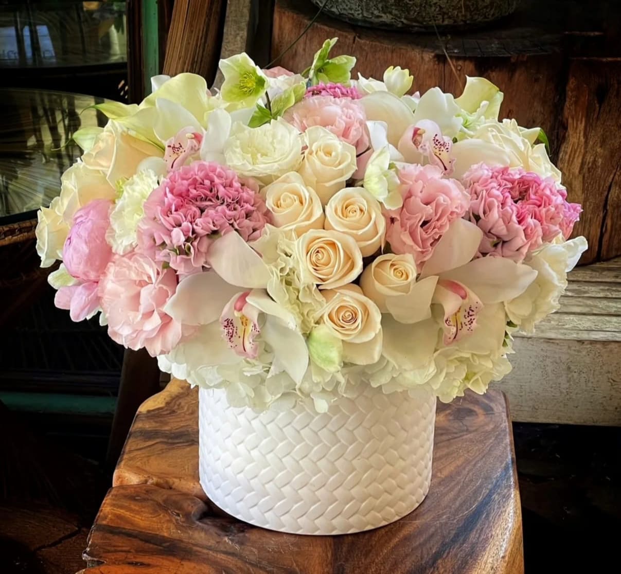 Low round arrangement of white and blush flowers in a white textured cylinder container